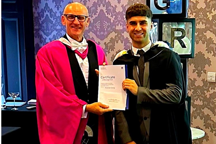 Student and lecturer in academic dress with degree certificate