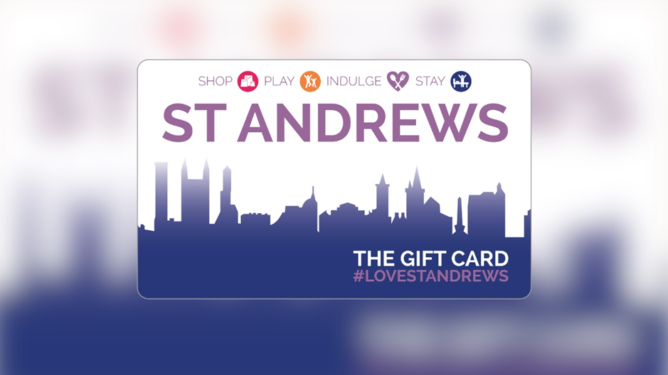 Graphic of a St Andrews-themed gift card design on a soft purple background. The card features a stylised skyline silhouette in gradient blue tones along the bottom and large text reading “ST ANDREWS.” Above this are icons and words “Shop,” “Play,” “Indulge,” and “Stay.” In the lower right corner, the text reads “The Gift Card #LoveStAndrews.”