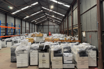 Warehouse packed with wrapped photocopiers and printers awaiting storage, refurbishment, or shipment.